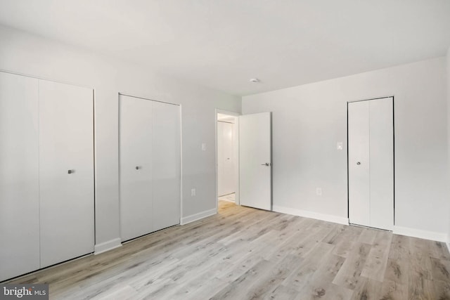 unfurnished bedroom featuring baseboards, light wood-type flooring, and multiple closets