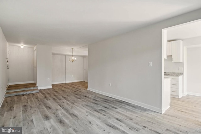 unfurnished living room with baseboards, a notable chandelier, and light wood-style flooring