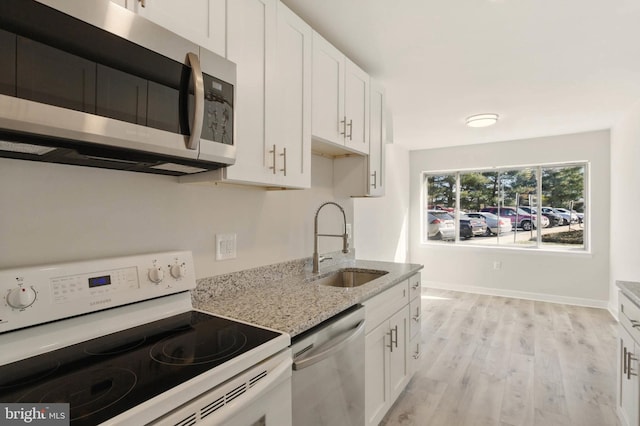 kitchen with light wood-style flooring, a sink, light stone counters, stainless steel appliances, and white cabinets