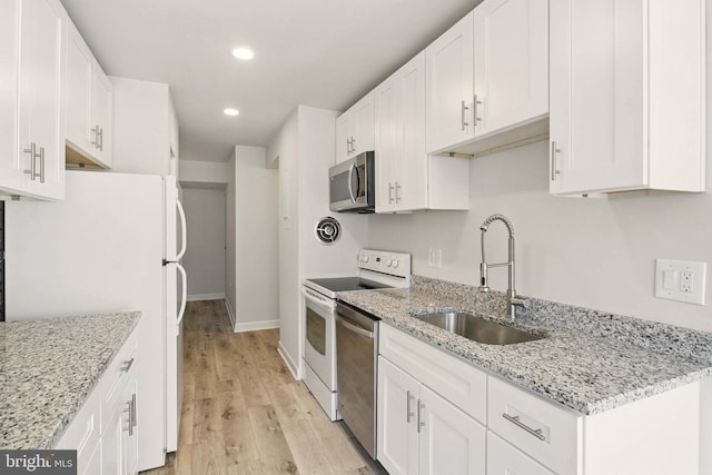 kitchen with light wood finished floors, appliances with stainless steel finishes, white cabinetry, and a sink