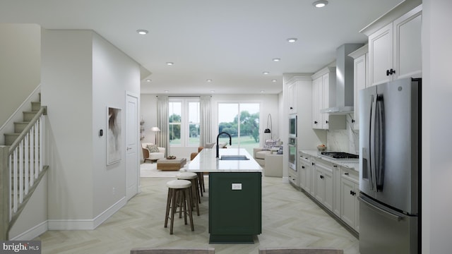 kitchen with a sink, wall chimney range hood, recessed lighting, stainless steel appliances, and a kitchen island with sink