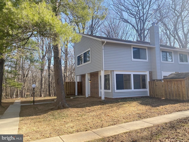 view of front of house featuring brick siding, a chimney, and fence