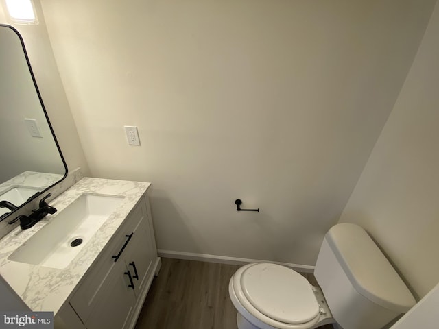 half bath featuring toilet, vanity, baseboards, and wood finished floors