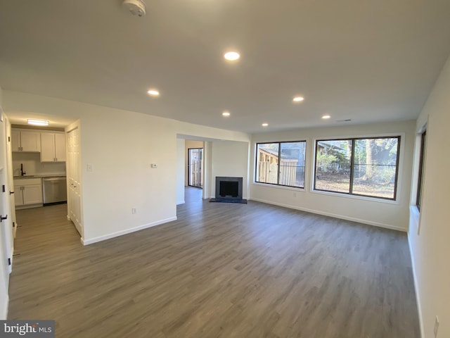 unfurnished living room featuring dark wood finished floors, a fireplace with raised hearth, recessed lighting, and baseboards