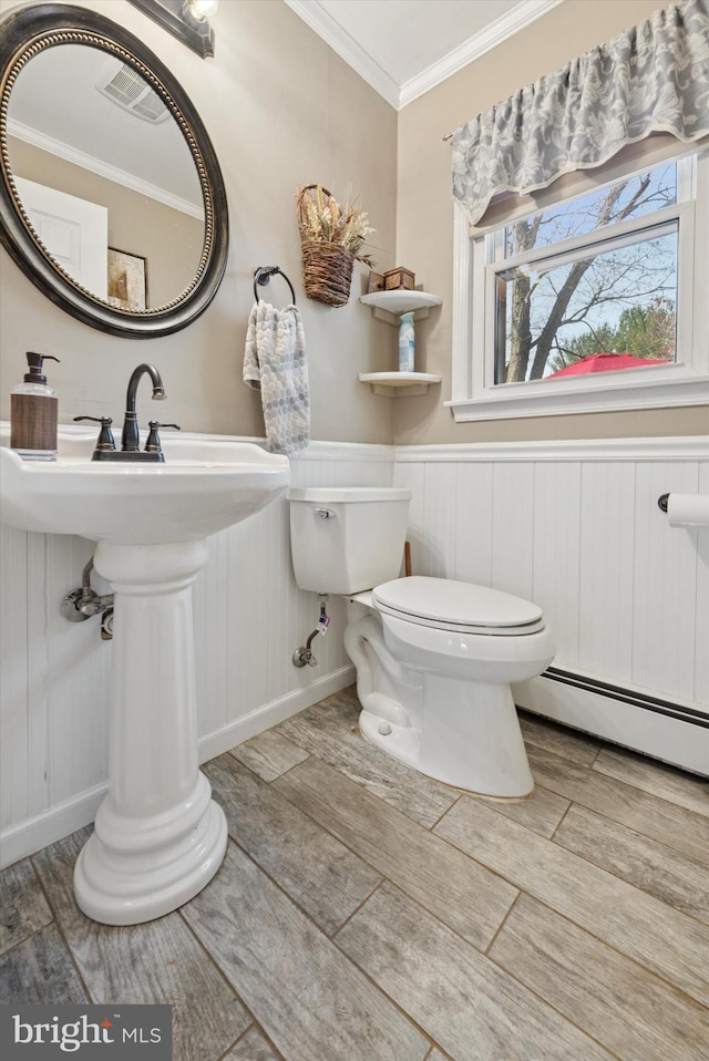 half bathroom featuring crown molding, wood finish floors, a wainscoted wall, toilet, and a baseboard radiator