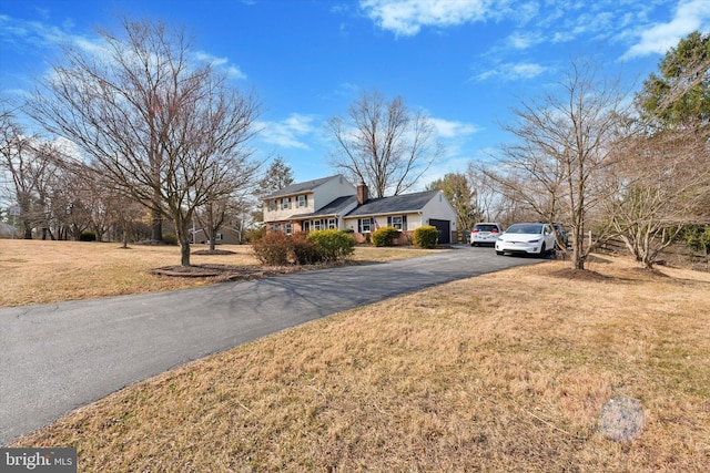 traditional-style house with aphalt driveway, a chimney, and a front lawn