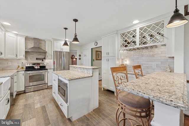 kitchen with wall chimney range hood, decorative backsplash, stainless steel appliances, light wood-style floors, and white cabinetry