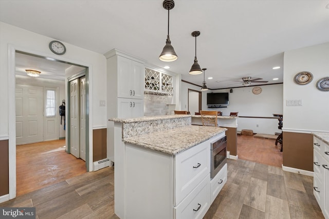 kitchen with wood finished floors, white cabinetry, a baseboard heating unit, stainless steel microwave, and a center island