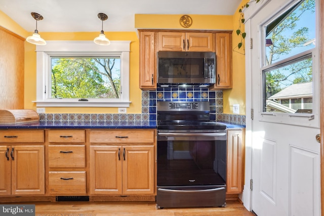 kitchen with dark countertops, light wood-style floors, stainless steel appliances, decorative light fixtures, and backsplash