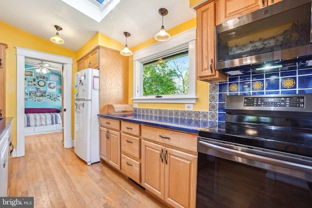 kitchen with dark countertops, lofted ceiling with skylight, light wood-style flooring, decorative light fixtures, and stainless steel appliances