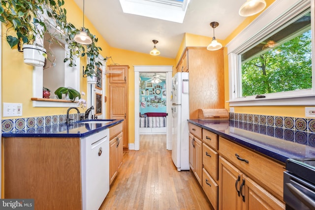 kitchen featuring dark countertops, a sink, white appliances, light wood-type flooring, and pendant lighting