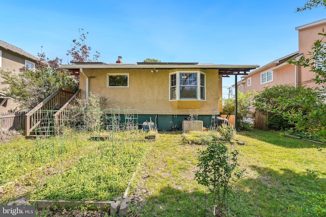 back of house with a lawn, fence, and stucco siding