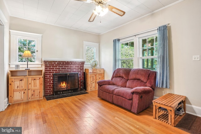 living area featuring wood-type flooring, a ceiling fan, crown molding, and a fireplace
