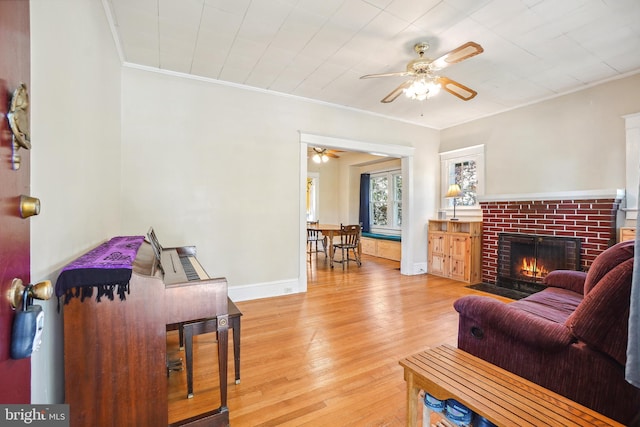 living area featuring crown molding, a fireplace, baseboards, a ceiling fan, and light wood finished floors