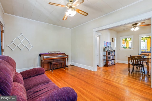 living area featuring light wood-style floors, a ceiling fan, baseboards, and crown molding