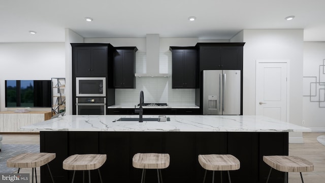 kitchen featuring decorative backsplash, appliances with stainless steel finishes, dark cabinetry, wall chimney exhaust hood, and a sink