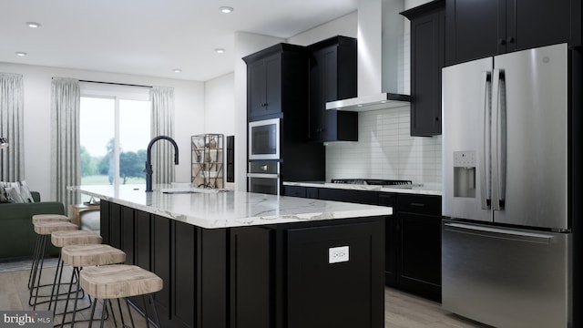 kitchen with dark cabinetry, stainless steel appliances, wall chimney exhaust hood, and a sink