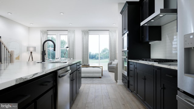 kitchen with wall chimney exhaust hood, dark cabinets, appliances with stainless steel finishes, and a sink