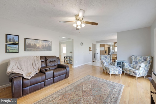 living area featuring a ceiling fan, baseboards, light wood-type flooring, and a textured ceiling