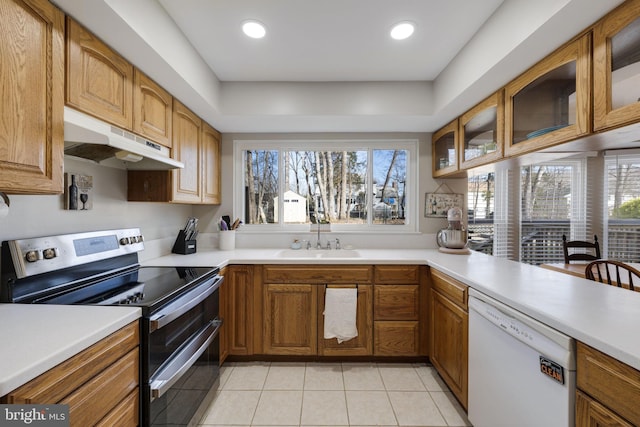 kitchen with under cabinet range hood, dishwasher, light countertops, range with two ovens, and a sink