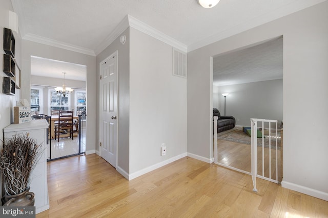 hall featuring visible vents, light wood-style floors, an inviting chandelier, and crown molding