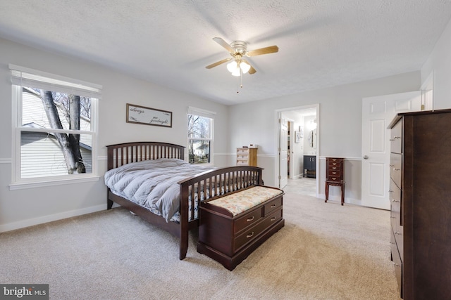 bedroom featuring baseboards, ceiling fan, a textured ceiling, light colored carpet, and connected bathroom