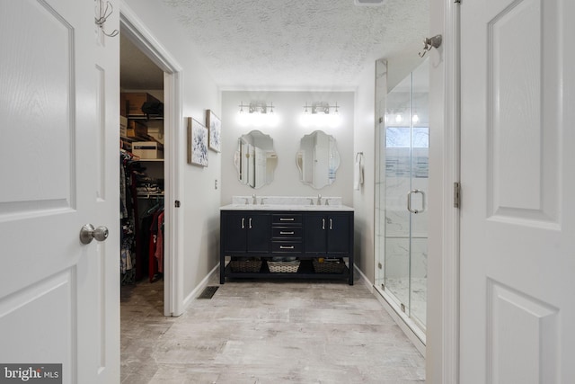 bathroom with a walk in closet, double vanity, a stall shower, a textured ceiling, and a sink