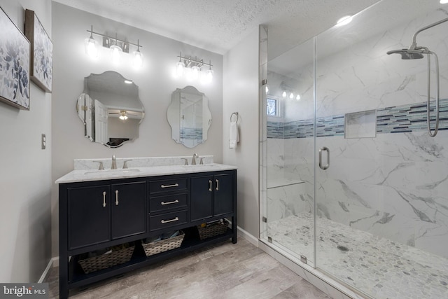 full bathroom with a marble finish shower, wood finished floors, a textured ceiling, and a sink