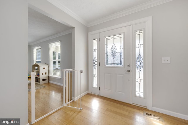 foyer entrance featuring visible vents, ornamental molding, baseboards, and hardwood / wood-style flooring