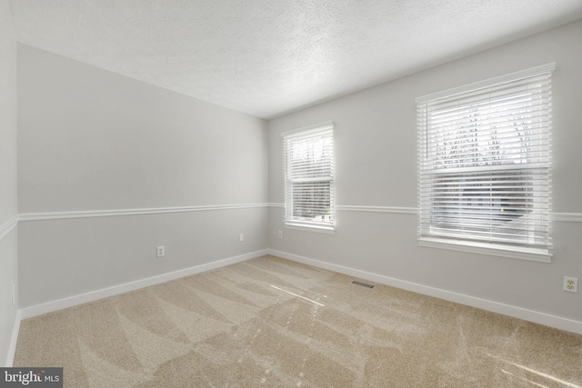 spare room featuring visible vents, carpet floors, a textured ceiling, and baseboards