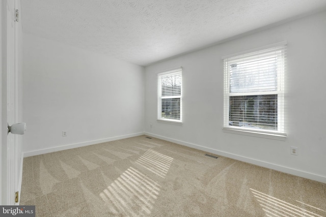 carpeted empty room featuring baseboards, visible vents, and a textured ceiling