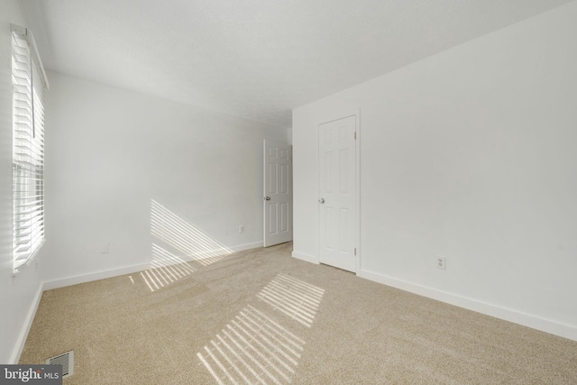 unfurnished room with light carpet, visible vents, and baseboards