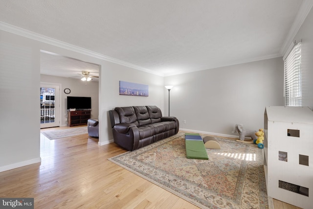 living area featuring ornamental molding, a ceiling fan, baseboards, and wood finished floors