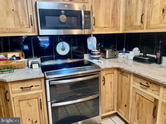 kitchen with light stone countertops, tasteful backsplash, appliances with stainless steel finishes, and light tile patterned flooring