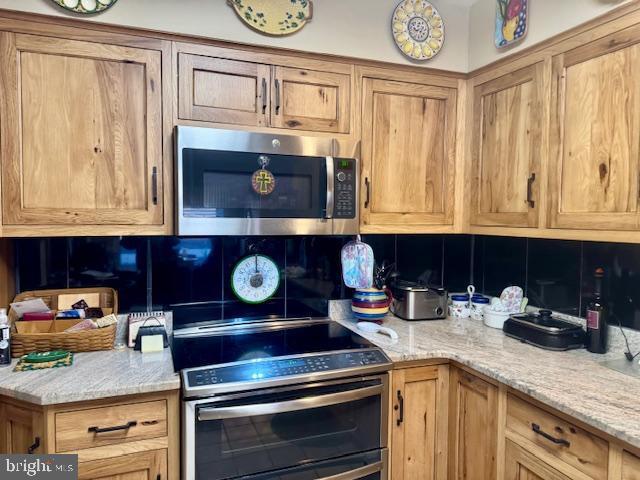 kitchen with stainless steel microwave, light stone counters, double oven range, and tasteful backsplash