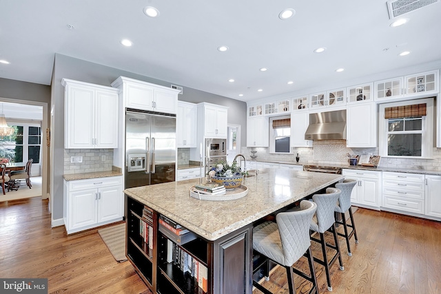 6813 Millwood Rd, Bethesda, MD 20817 - kitchen with built in appliances, range hood, tasteful backsplash, white cabinets, and a kitchen island with sink