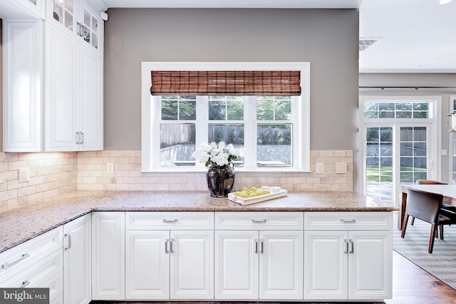 6813 Millwood Rd, Bethesda, MD 20817 - kitchen featuring white cabinets, glass insert cabinets, light stone countertops, tasteful backsplash, and wood finished floors