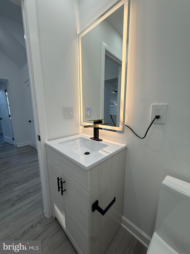 half bathroom with vanity, toilet, wood finished floors, and baseboards