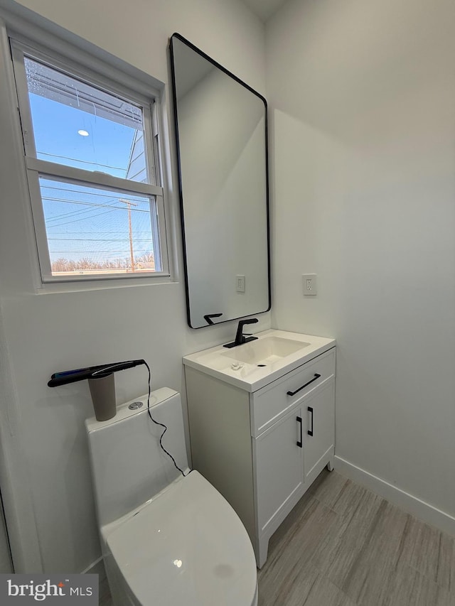 bathroom featuring baseboards, toilet, wood finished floors, and vanity