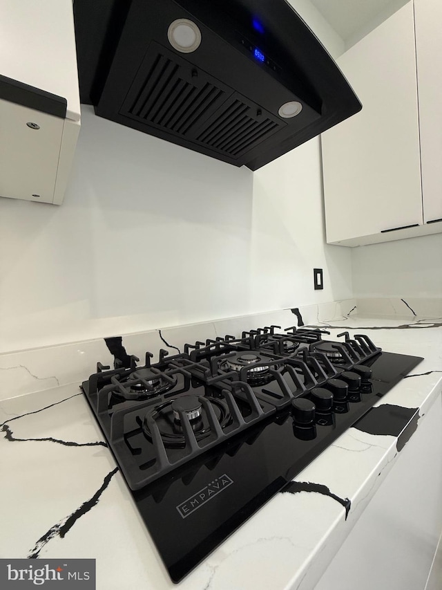 room details featuring extractor fan, white cabinets, and black gas cooktop