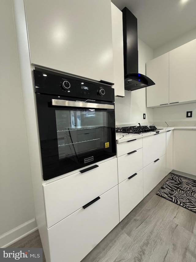 kitchen featuring light wood finished floors, black appliances, light countertops, exhaust hood, and white cabinetry