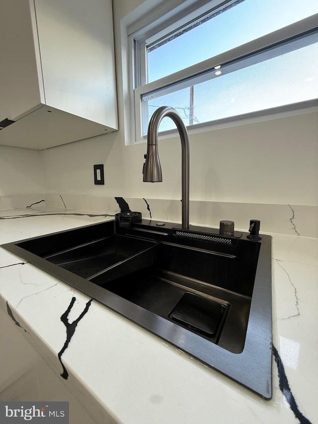 details featuring white cabinets, light stone countertops, and a sink