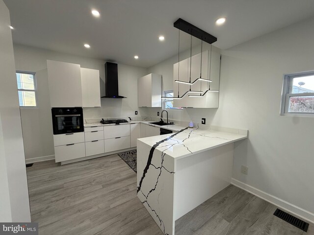 kitchen with visible vents, oven, a peninsula, wall chimney exhaust hood, and gas cooktop