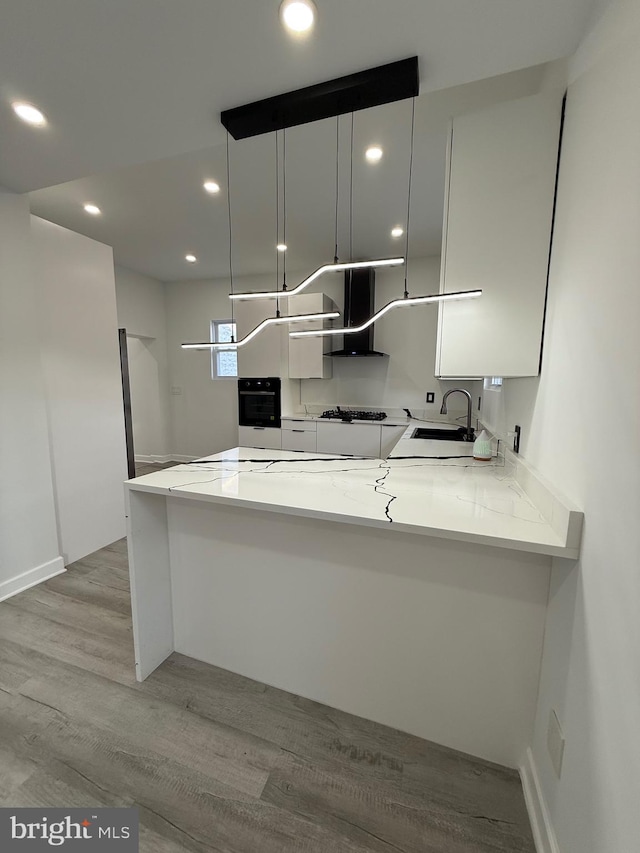 kitchen featuring a sink, black oven, white cabinetry, a peninsula, and light wood finished floors