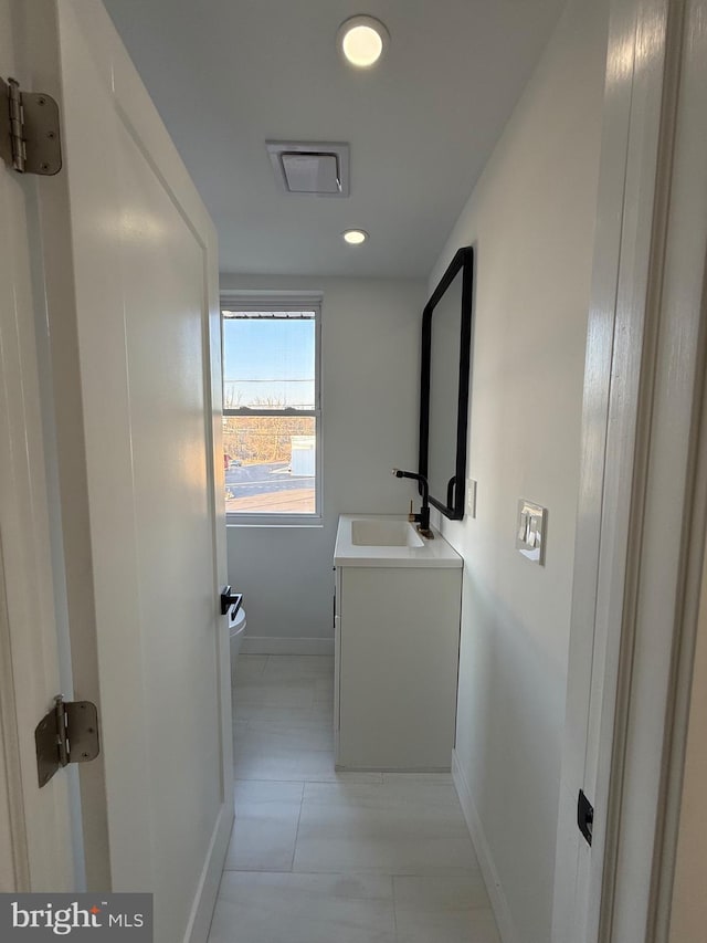 hallway featuring recessed lighting, baseboards, and a sink