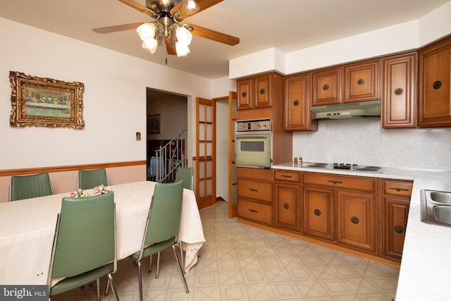 kitchen featuring under cabinet range hood, electric cooktop, oven, and brown cabinets