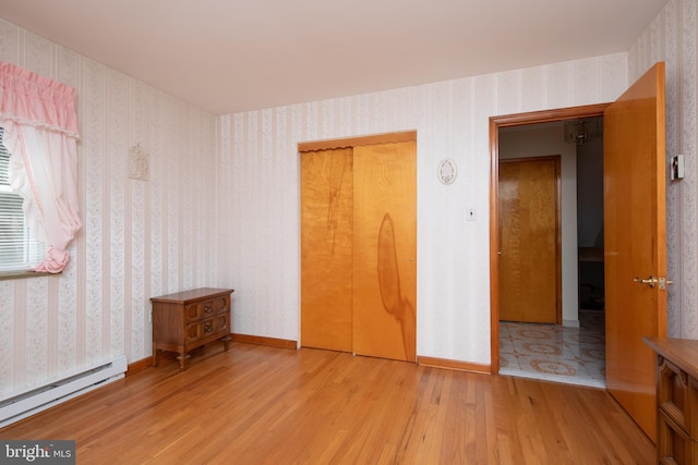 unfurnished bedroom with baseboard heating, wood finished floors, and wallpapered walls