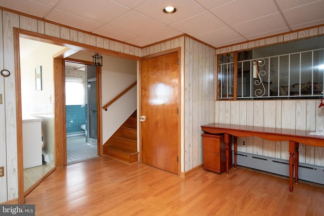 interior space featuring a drop ceiling, baseboard heating, wood finished floors, and wooden walls