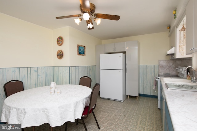 dining space featuring a ceiling fan, light floors, and wainscoting