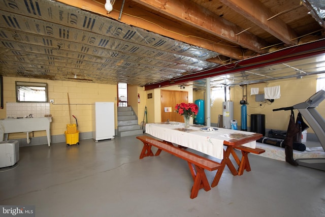 below grade area featuring water heater, concrete block wall, and stairs